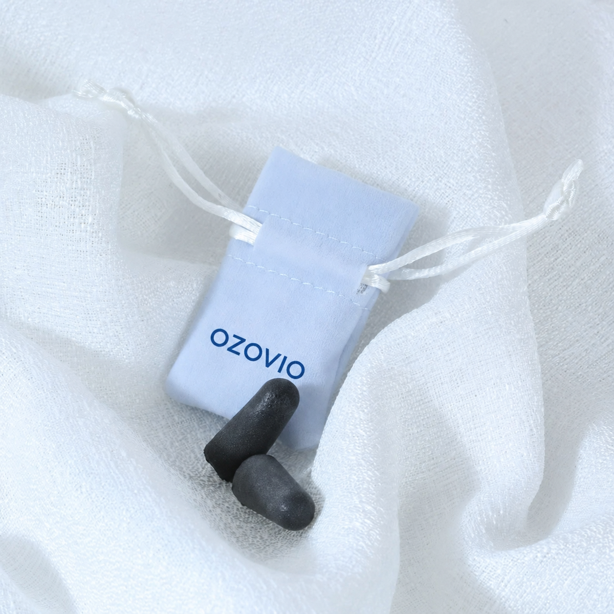 Bouchons anti-bruit OZOVIO en mousse avec leur pochette en tissu bleu clair, posés sur un drap blanc