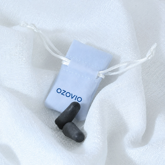 Bouchons anti-bruit OZOVIO en mousse avec leur pochette en tissu bleu clair, posés sur un drap blanc